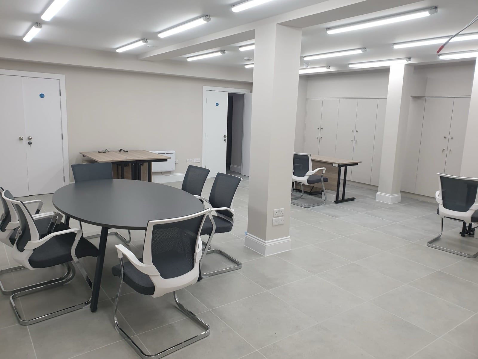 Finished open-plan commercial room with pale walls, ceiling lighting, and meeting tables.