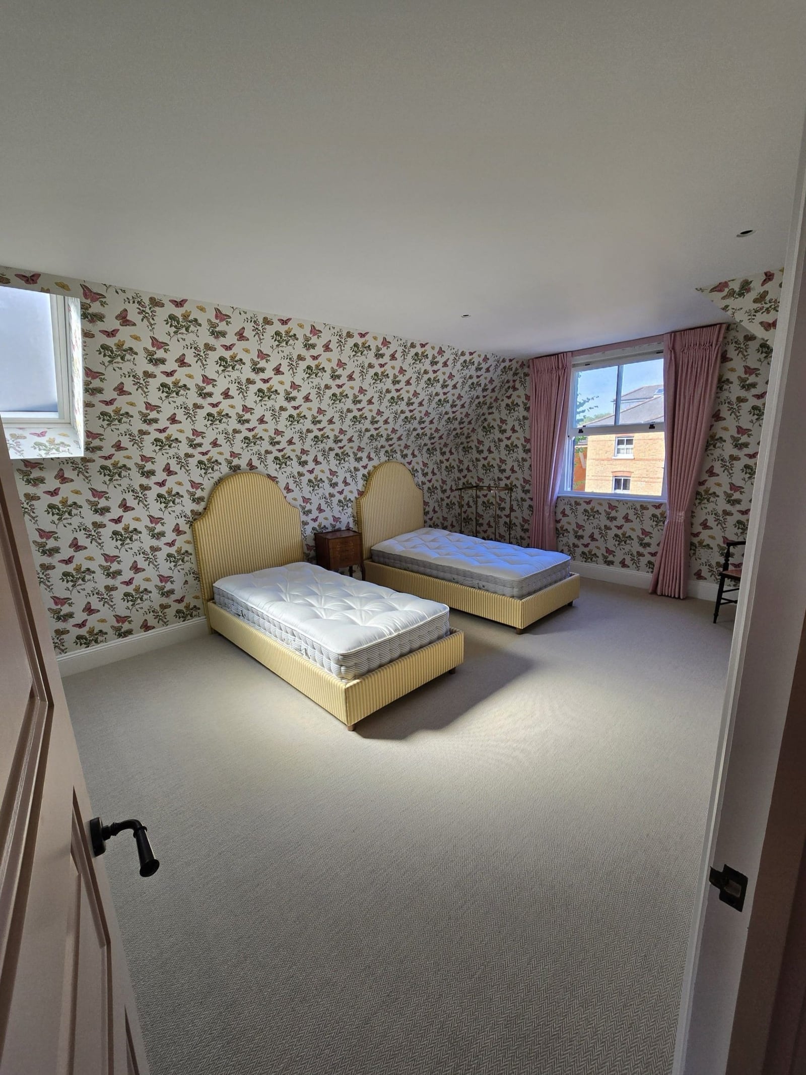 Twin bedroom finished with floral wallpaper, twin beds, and pink curtains.
